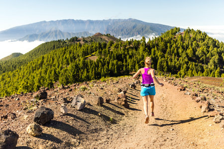 Young woman cross country running in mountains on sunny summer day  Beauty female runner jogging and exercising outdoors in nature, rocky trail footpath on La Palma, Canary Islandsの写真素材