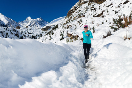 Woman running on white snow in Himalaya Mountains in Nepal. Adventure cross country runner on snow trail in beautiful mountain landscape.の写真素材