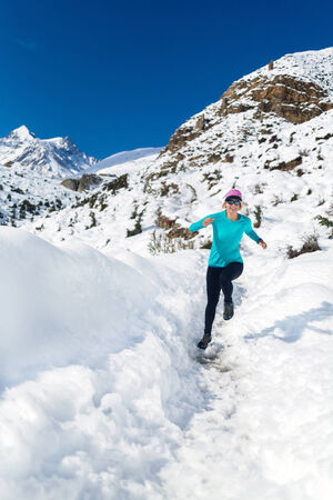 Woman running on white snow in Himalaya Mountains in Nepal. Adventure cross country runner on snow trail in beautiful mountain landscape.の写真素材