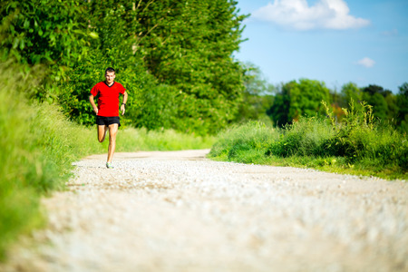 Man runner running on country road in summer sunset. Young athlete male training and doing workout outdoors in nature.の写真素材