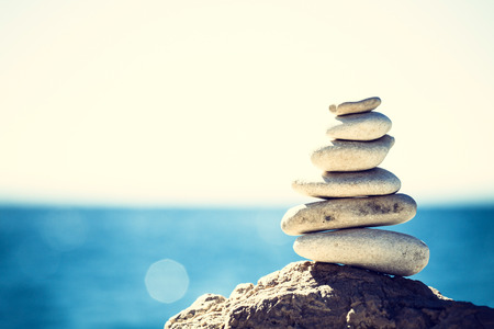 Stones balance, vintage retro instagram like hierarchy stack over blue sea background. Spa or well-being, freedom and stability concept on rocks.の写真素材