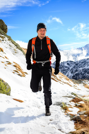 Young man trail running in mountains on winter or fall sunny day. Male athlete cross country runner training for ultra distance outdoors in cold snow nature.の写真素材