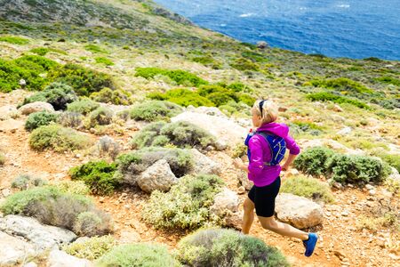 Trail running woman cross country running in mountains on a beautiful summer day. Training and working out a runner jogging and exercising outdoors in nature rocky footpath on Crete Greeceの写真素材
