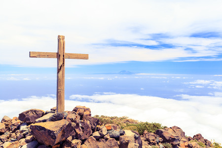Christian wooden cross on mountain top, rocky summit, beautiful inspirational landscape with ocean, island, clouds and blue sky, looking at scenic blue sea and white clouds.の写真素材