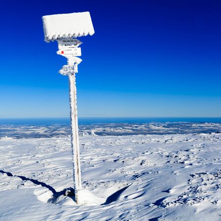 Sign and arrows in winter white mountains on snow. Inspirational mountains landscape in cold winter, hiking trail information and signs.の写真素材