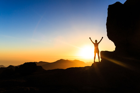 Woman successful hiking climbing silhouette in mountains, motivation and inspiration in beautiful sunset and ocean. Female hiker with arms up outstretched on mountain top looking at beautiful night sunset inspirational landscape.の写真素材