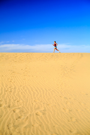 Young woman running on beautiful inspirational desert dunes on sunny summer day. Beauty female runner jogging and exercising outdoors in nature Gran Canaria, Canary Islandsの写真素材