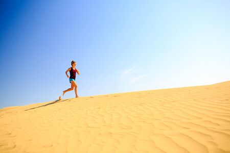 Young woman running on beautiful inspirational desert dunes on sunny summer day. Beauty female runner jogging and exercising outdoors in nature Gran Canaria, Canary Islandsの写真素材