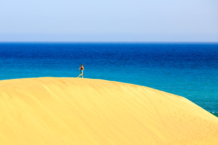 Young woman running on beautiful inspirational beach desert dunes on sunny summer day. Beauty female runner jogging and exercising, inspiration and motivation outdoors in nature on Gran Canaria beach, Canary Islandsの写真素材