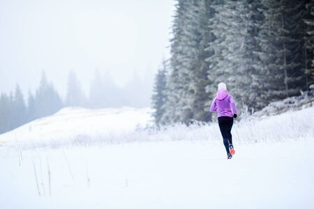 Sport, fitness inspiration and motivation. Young happy woman cross country running in mountains on snow, winter day. Female trail runner jogging exercising outdoors in white environemnt.の写真素材
