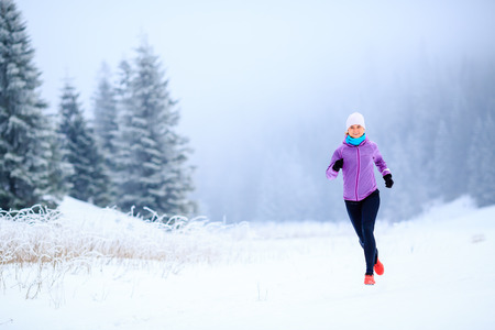 Sport, fitness inspiration and motivation. Young happy woman cross country running in mountains on snow, winter day. Female trail runner jogging exercising outdoors.の写真素材