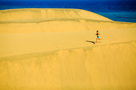 Young woman running on beautiful inspirational desert dunes on sunny summer day. Beauty female runner jogging and exercising outdoors in nature Gran Canaria, Canary Islandsの写真素材