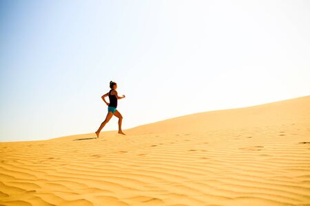 Young woman running on beautiful inspirational desert dunes on sunny summer day. Beauty female runner jogging and exercising outdoors in nature Gran Canaria, Canary Islandsの写真素材