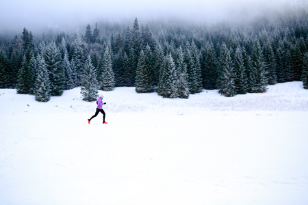 Winter running woman. Sport, fitness, jogging inspiration and motivation. Young happy woman cross country running in mountains on snow, winter day. Female trail runner working out, jogging exercising.の写真素材