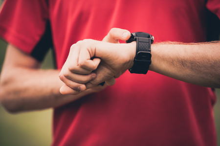Runner using heart rate monitor training running, smartwatch checking performance or GPS. Man athlete looking at stopwatch. Healthy runner closeup on trail running workout. Wearable technology for tracking activity.の写真素材