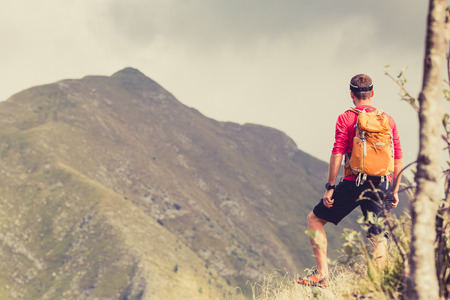 Hiking man, backpacker, climber or trail runner in mountains looking at beautiful inspirational landscape view. Fitness and healthy lifestyle outdoors in summer natureの写真素材