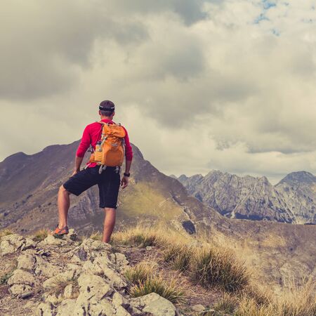 Hiking man, backpacker, climber or trail runner in mountains looking at beautiful inspirational landscape view. Fitness and healthy lifestyle outdoors in summer natureの写真素材