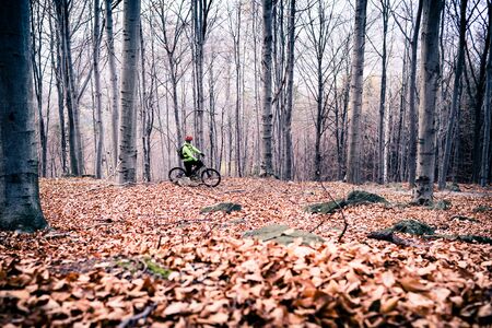 Mountain biker on cycle trail in woods. Mountains in winter or autumn landscape forest. Man cycling MTB on rural country road. Sport fitness motivation and inspiration.の写真素材