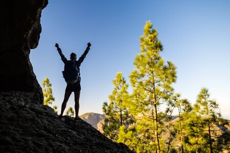Woman successful hiking climbing silhouette in mountains, motivation and inspiration in beautiful sunset and ocean. Female hiker with arms up outstretched on mountain top looking at beautiful night sunset inspirational landscape.の写真素材