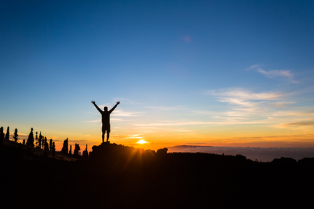 Man hiker silhouette with arms outstretched in mountains. Male runner or climber looking at sunset view. Business concept and hands up and enjoy inspirational landscape, rocky trail footpath on Tenerife, Canary Islandsの写真素材