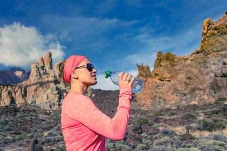 Trail runner woman drinking water and running in mountains, inspirational landscape. Training and working out jogging and exercising outdoors in nature, rocky footpath on Canary Islands, Spainの写真素材