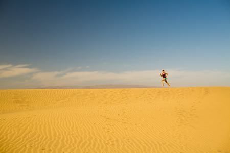 Young woman running on beautiful inspirational desert dunes on sunny summer day. Female runner training and working out, jogging and exercising outdoors in nature, Gran Canaria, Canary Islands Spain.の写真素材