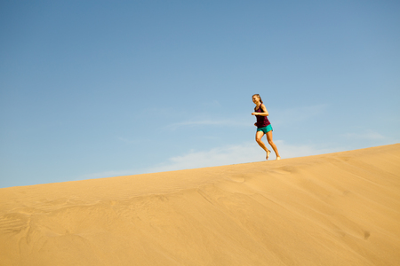 Young woman running on beautiful inspirational desert dunes on sunny summer day. Female runner training and working out, jogging and exercising outdoors in nature, Gran Canaria, Canary Islands Spain.の写真素材