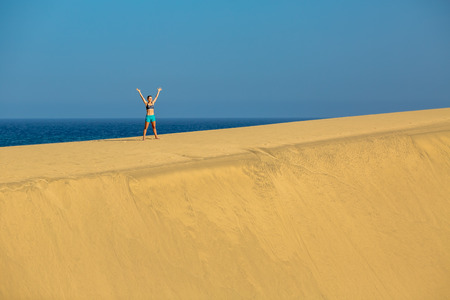 Woman with arms up outstretched on sand desert dunes running on beautiful inspirational desert dunes on sunny summer day. Female athlete runner jogging and exercising outdoors in nature Gran Canaria, Canary Islandsの写真素材