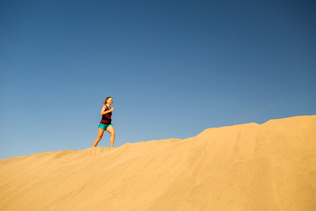 Young woman running on beautiful beach, inspirational desert dunes on sunny day. Female runner training and working out, jogging and exercising outdoors, Gran Canaria, Canary Islands Spain.の写真素材