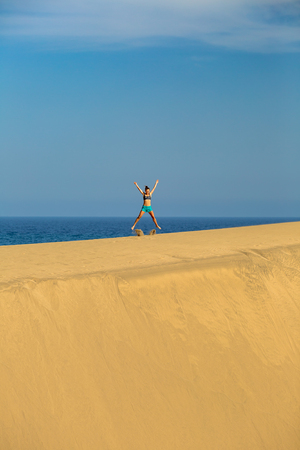 Woman with arms up outstretched on sand desert dunes running on beautiful inspirational desert dunes on sunny summer day. Female athlete runner jogging and exercising outdoors in nature Gran Canaria, Canary Islandsの写真素材
