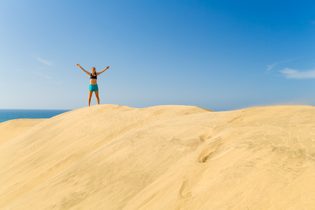 Fitness successful happy woman with arms up outstretched celebrating on beautiful inspirational beach dunes on summer day. Beauty female runner training and exercising outdoors, business concept.の写真素材
