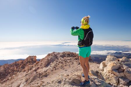 Hiking woman taking pictures in mountains with smart phone.  Using smartphone outdoors. Fitness and healthy lifestyle outdoors in summer nature on Tenerife, Canary Islands.の写真素材