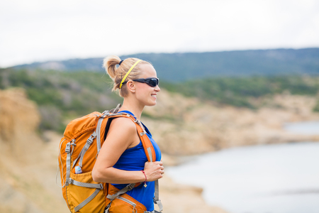 Woman hiking on trail with backpack at seaside on island. Recreation and healthy lifestyle outdoors in summer mountains. Trekking and activity concept in beautiful inspirational landscape.の写真素材