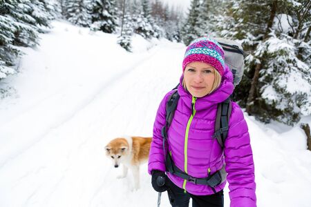 Woman hiking in white winter forest woods with akita dog. Recreation fitness and healthy lifestyle outdoors in nature. Motivation and inspirational winter landscape.の写真素材