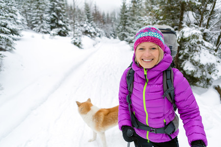 Woman hiking in white winter forest woods with akita dog. Young girl walking on snowy trail. Recreation fitness and healthy lifestyle outdoors in nature. Motivation and inspirational winter landscape.の写真素材