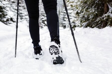 Female backpacker hiking in white winter woods on snow trail. Legs and boots trekking. Recreation fitness and healthy lifestyle outdoors in nature. Motivation and inspiring winter landscape.の写真素材