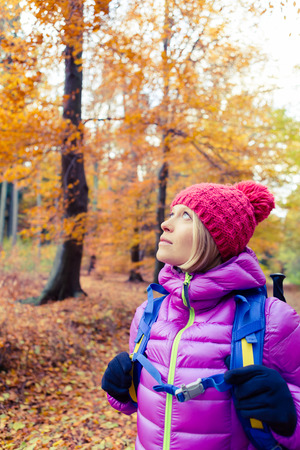 Hiking woman with backpack looking up at inspirational autumn golden trees.Fitness travel and healthy lifestyle outdoors in fall season nature. Female backpacker tourist walking in forest.の写真素材