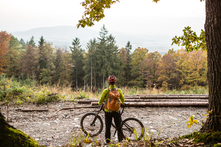 Mountain biker looking at inspiring mountain landscape, standing with bicycle. Man cycling MTB on dirty road in woods. Sport and active recreation, fitness motivation and inspiration.の写真素材