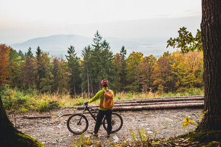 Mountain biker looking at inspiring mountain landscape, standing with bicycle. Man cycling MTB on dirty road in woods. Sport and active recreation, fitness motivation and inspiration.の写真素材