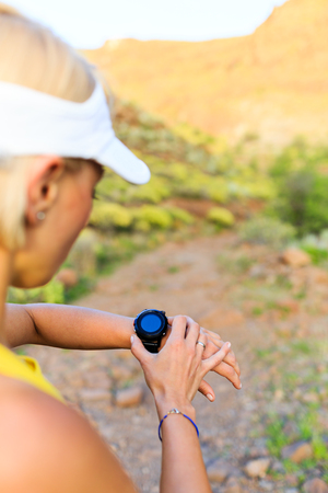 Woman runner checking the elevation on sports watch, smartwatch with altimeter app in summer mountains. Young girl training and running on mountain trail in the morning.の写真素材
