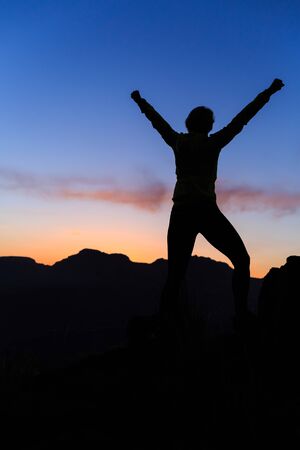 Woman hiking silhouette in mountains, sunset and ocean. Female hiker, climber or trail runner with arms outstretched on mountain top looking at beautiful night sunset inspirational landscape.の写真素材