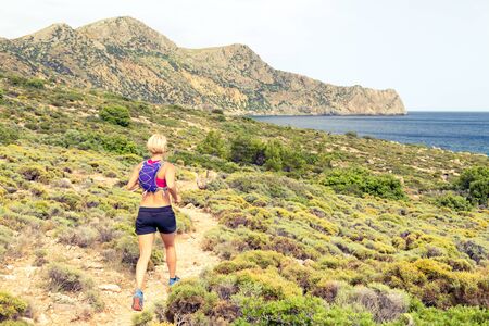 Trail running woman cross country running in mountains on summer beautiful day. Training and working out runner jogging and exercising outdoors in nature, rocky footpath on Crete, Greeceの写真素材