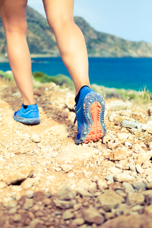 Hiking or running woman in beautiful mountains inspirational landscape. Sole of sports shoe and legs on rock trail. Hiker trekking or walking of footpath. Healthy fitness lifestyle outdoors.の写真素材