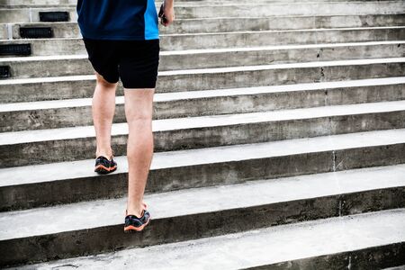 Man runner running on concrete stairs in city. Young male athlete training and doing workout outdoors in city. Endurance training, fitness and exercising outdoors in urban environment.の写真素材