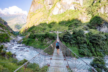 Woman backpacker crossing suspension bridge in Himalayas Nepal. Trekking and hiking with backpack in high mountains. Annapurna Himal Range on Annapurna Circuit Trek. Autumn season in Nepal, Asia.の写真素材