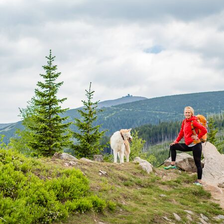 Woman hiking with akita inu dog on mountain trail. Recreation and healthy lifestyle outdoors, summer in mountains and woods, inspirational nature. Fitness, sport, trekking and activity concept.の写真素材