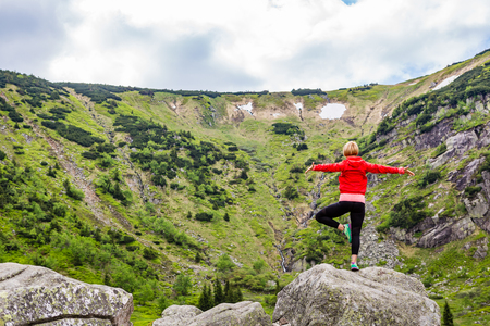 Woman meditating in yoga pose in front of mountain lake. Female hiker relaxing in beautiful inspirational mountains landscape. Healthy lifestyle outdoors in nature concept.の写真素材