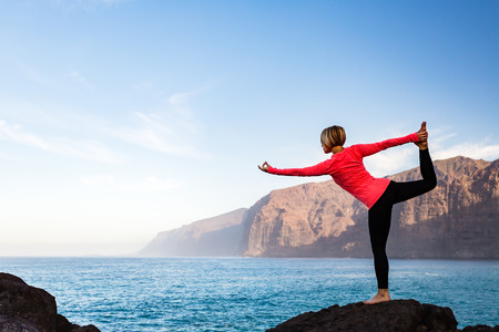 Woman meditating in yoga dancer pose(Natarajasana) over ocean and islands, coastline and rocky mountains. Inspiration and  motivation with healthy lifestyle in beautiful sunset landscape, fitness concept.の写真素材