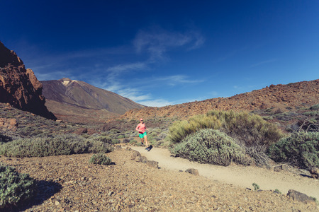 Young woman running in mountains on sunny summer day. Beauty female runner jogging and exercising outdoors in nature, trail running training on rocky trail footpath on Tenerife, Canary Islandsの写真素材