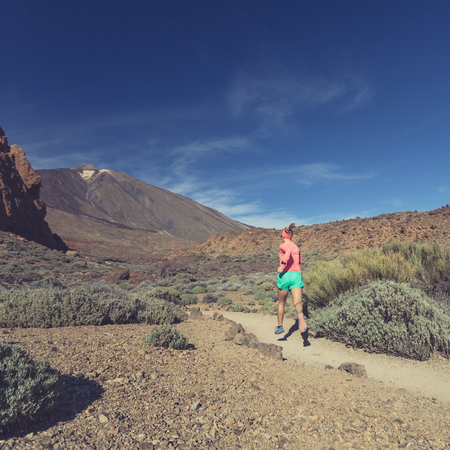 Young woman trail running in mountains on sunny summer day. Female runner jogging and working out in nature, cross country running on rocky trail footpath on Tenerife, Canary Islandsの写真素材